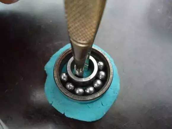 用鑷子或別的相近的物體越過內圈，同時向滾珠的方向用力頂住